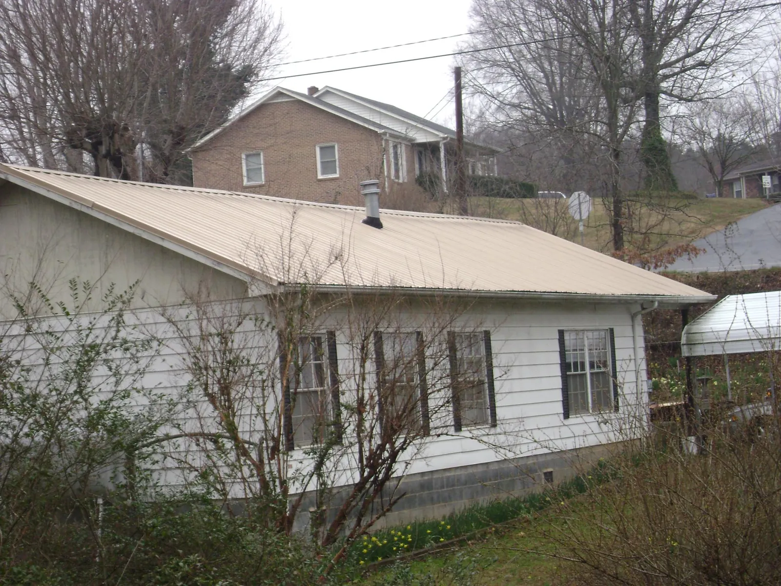 Tan metal roof on a white sided house set into a hillside — Commercial Roofing by Roofing Brothers in Whitewater
